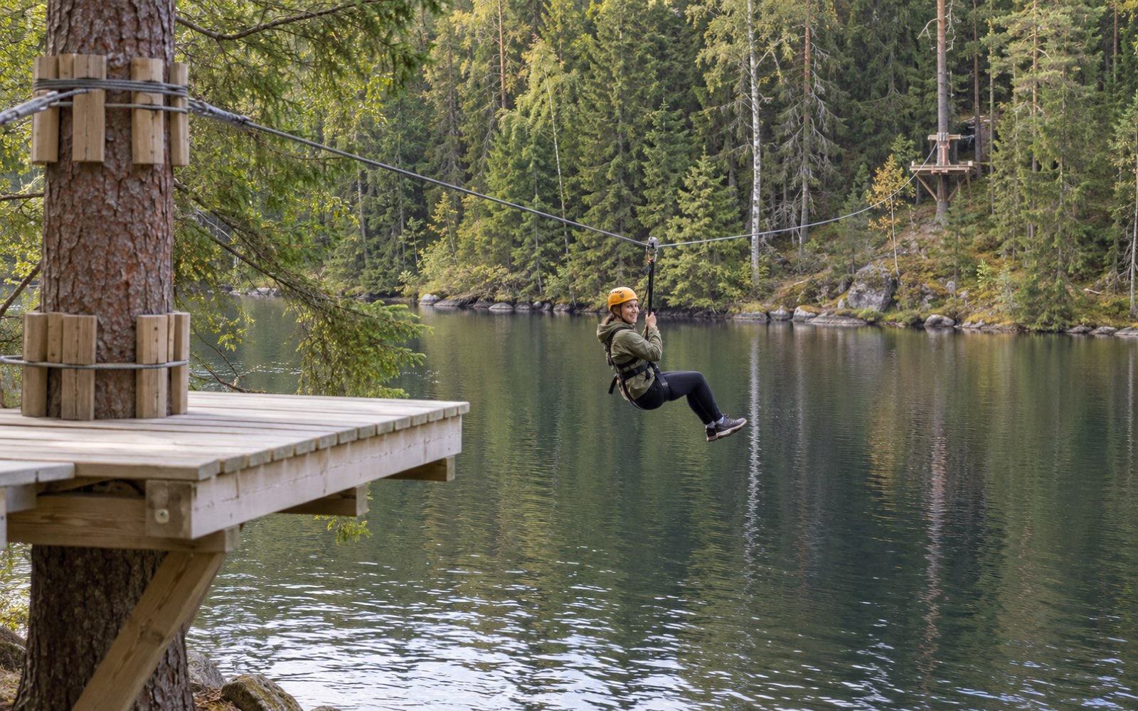 A climber in a yellow helmet on the zip line over the forest lake